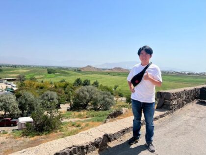 Yuki Kusakabe standing on a stone terrace overlooking green fields of the Ararat plain
